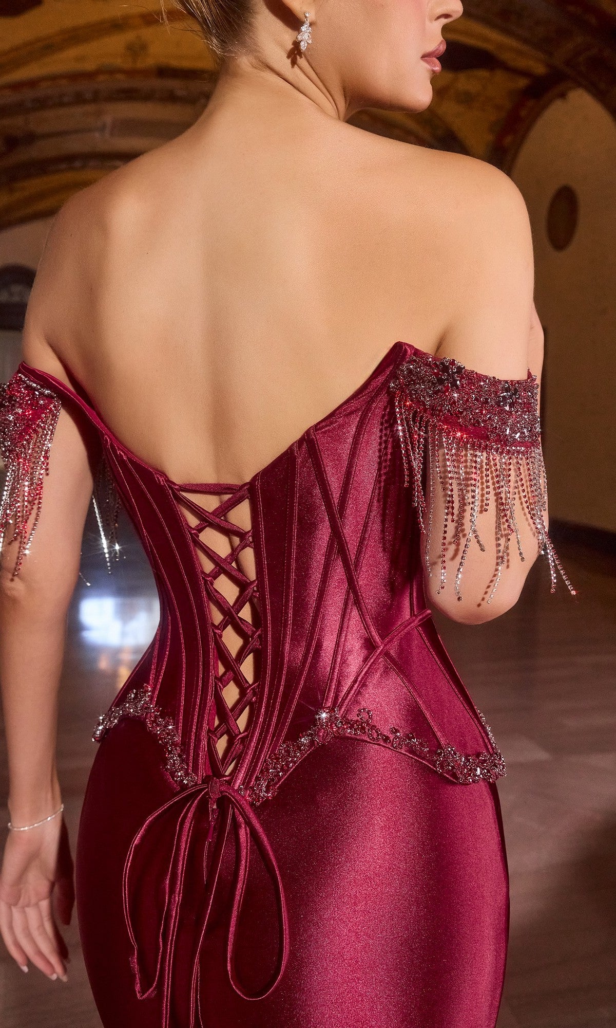 Woman wearing the Ladivine CD688 long prom dress, an off-the-shoulder maroon satin corset gown featuring crystal embellishments and beaded fringe on the sleeves.